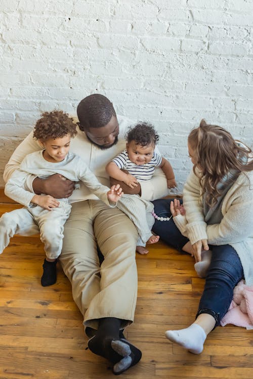 Free From above multiracial parents with boy and little baby sitting on floor near wall while spending time together in light room Stock Photo