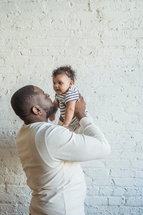 Man in White Long Sleeve Shirt Carrying a baby in Stripe Shirt