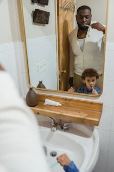 A father and son bonding while brushing teeth together in a cozy bathroom.
