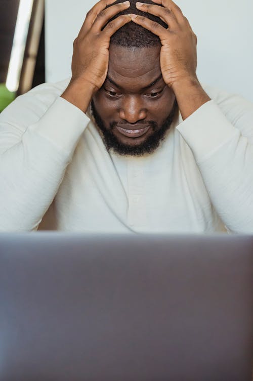 Sad black man with hands on head near laptop