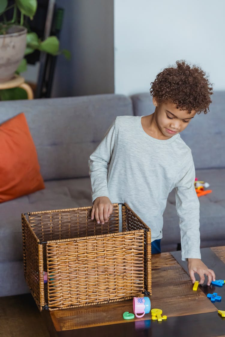 Black Child Near Table With Toy Box In Apartment