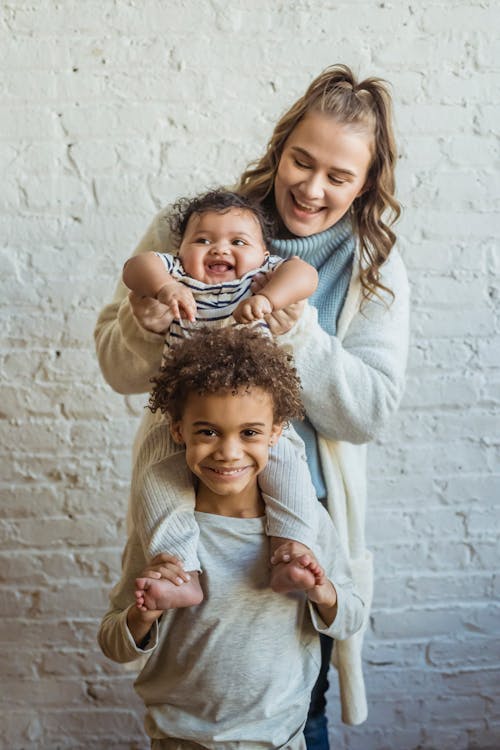 Happy mother with ethnic kids standing against brick wall