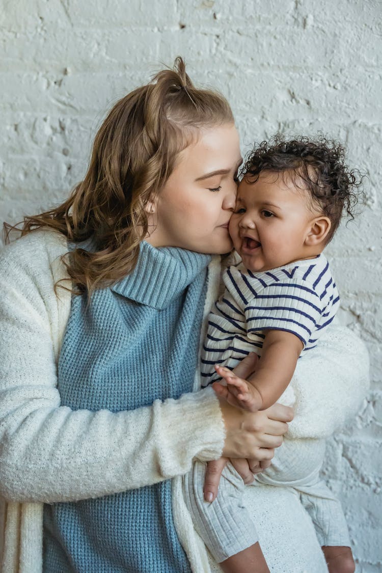 Young Mother Carrying And Kissing Ethnic Baby On Cheek