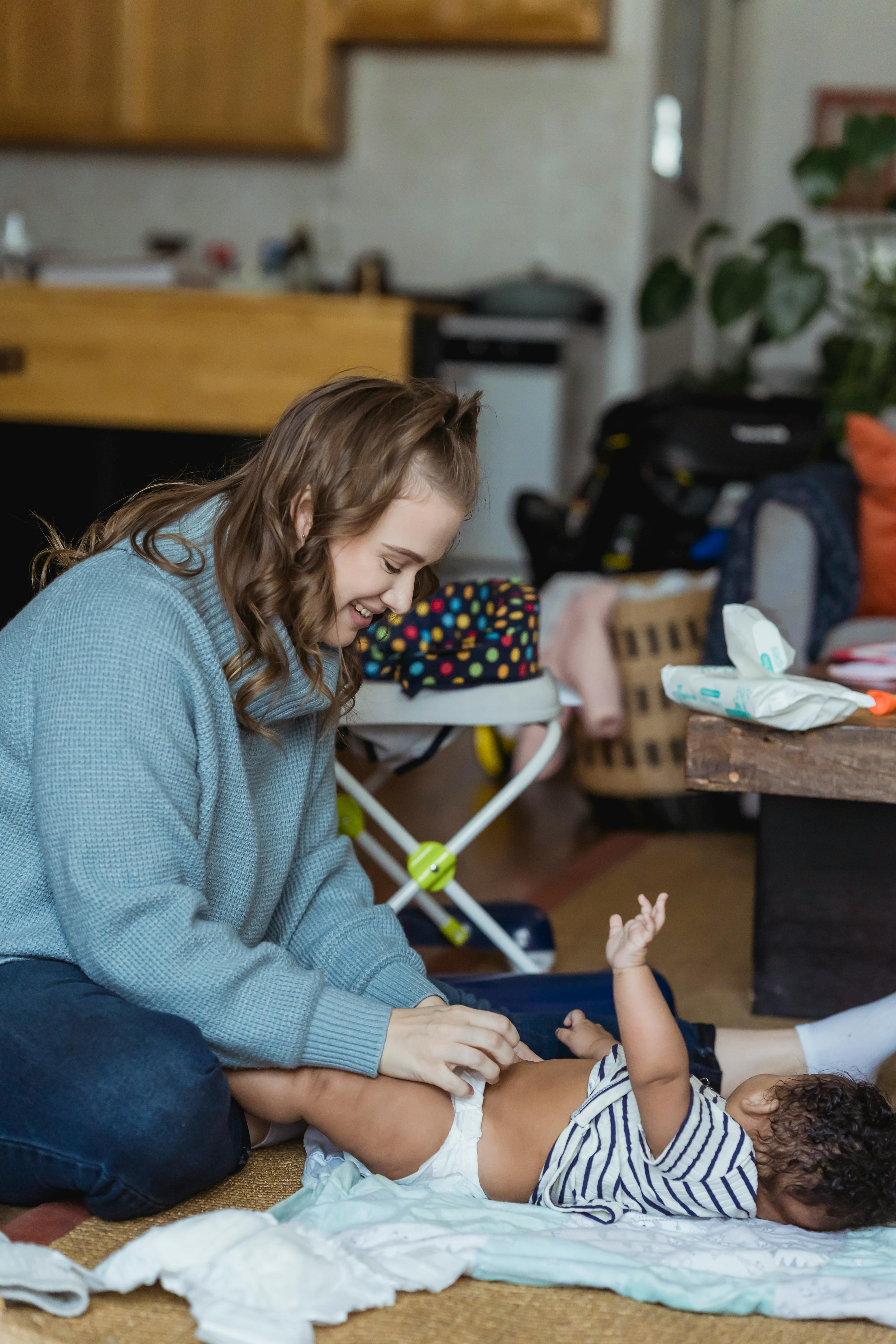 cheerful mother changing diaper for ethnic baby