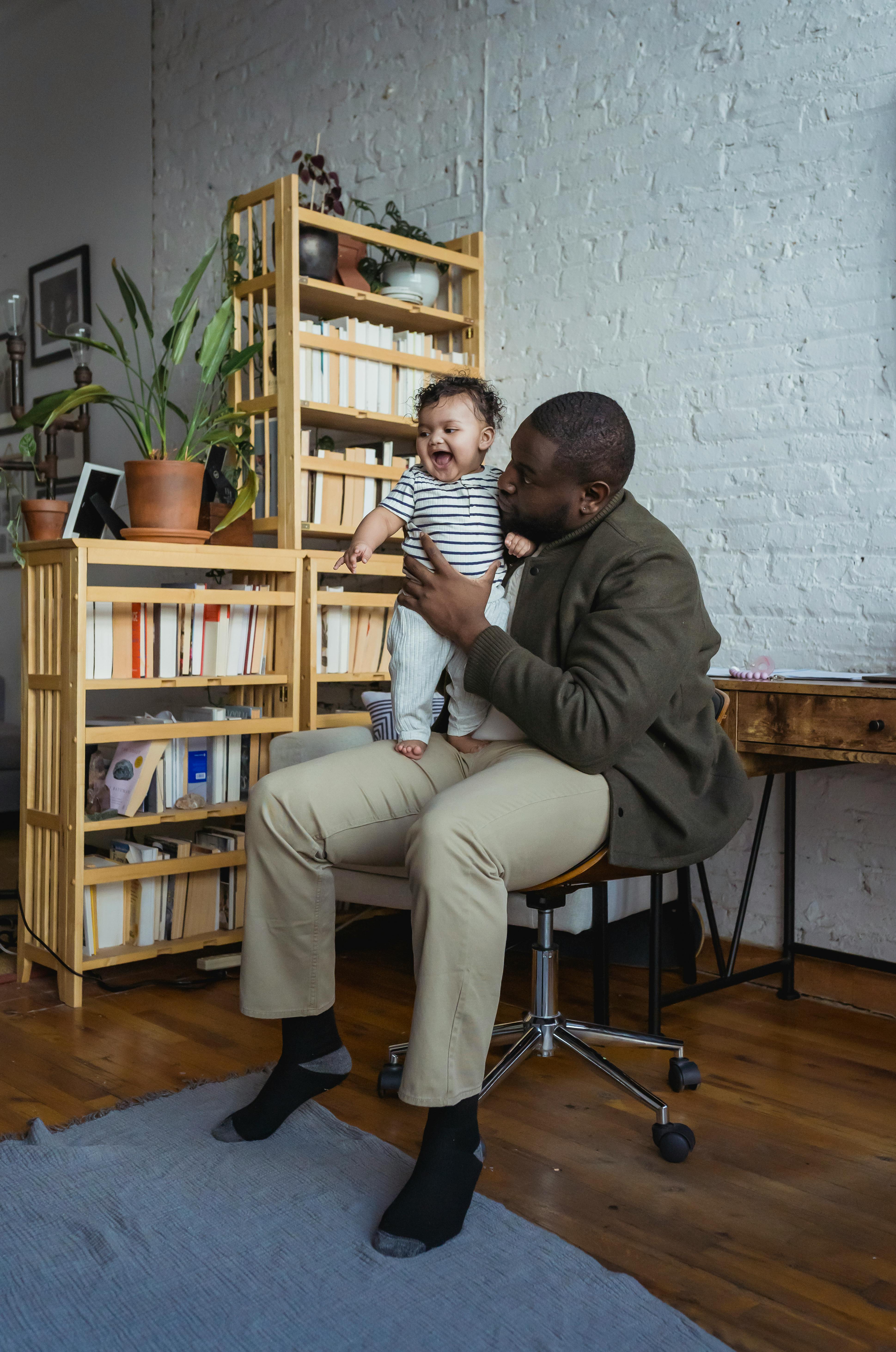 black father playing with cute baby and sitting on chair