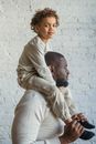 Side view focused African American male in casual wear carrying content son on shoulders against white wall in light room