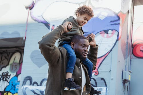 Black father carrying adorable son on shoulders on street