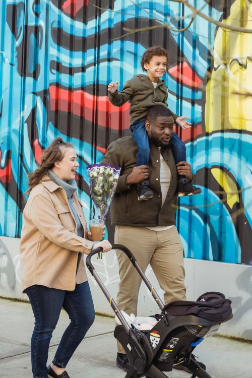 Free Happy woman with baby stroller walking on street near black husband carrying cheerful son on shoulders Stock Photo