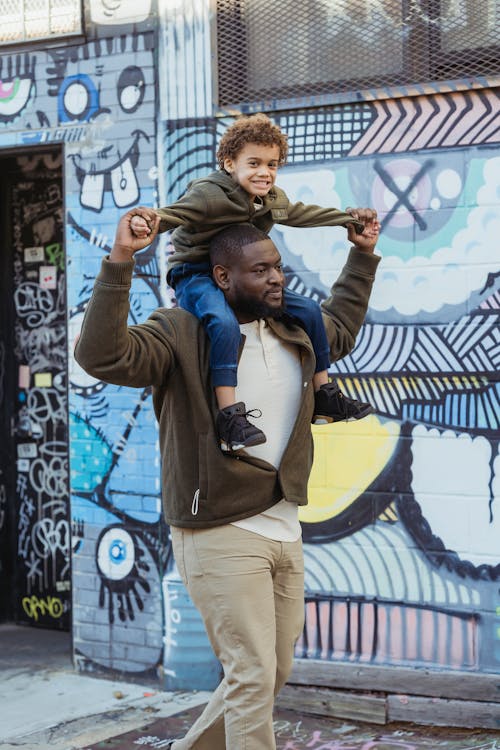 Content black father carrying son on shoulders on street