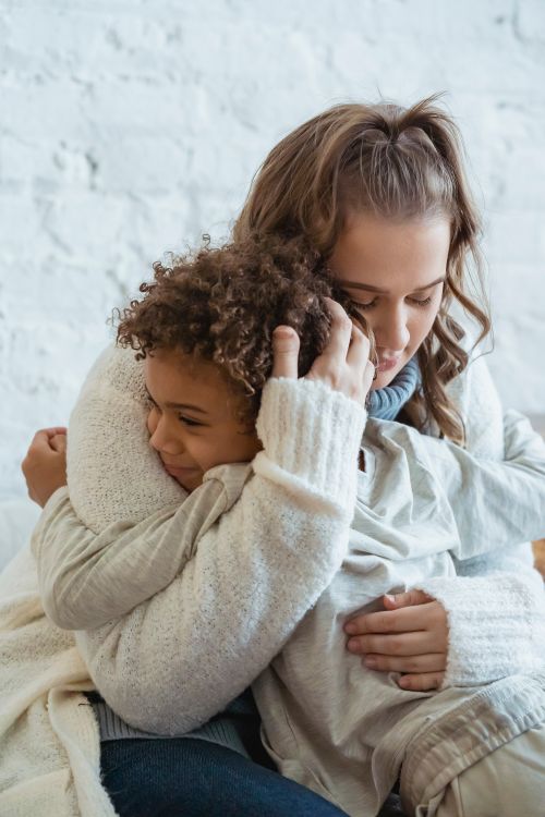 Free Caring young mother gently embracing positive ethnic son against white wall in living room Stock Photo