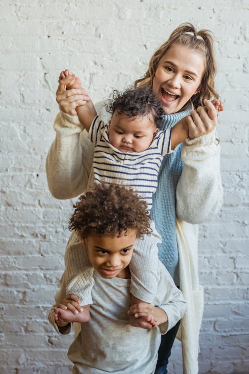 Free Cheerful smiling mon with cute African American toddler and boy near white brick wall Stock Photo