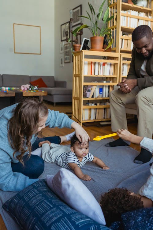 Crop African American father watching mother playing with cute little toddler on floor at home