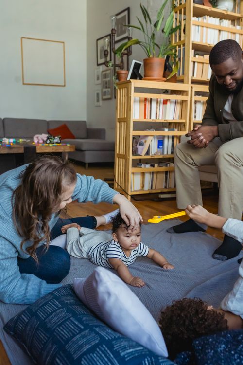 Free Crop African American father watching mother playing with cute little toddler on floor at home Stock Photo