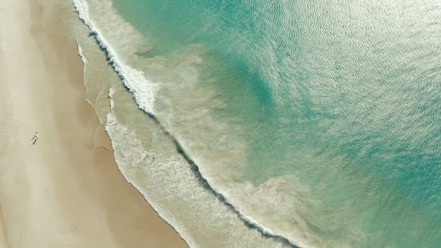 A serene aerial view of sandy shores and turquoise ocean waves in Cape Town, South Africa.