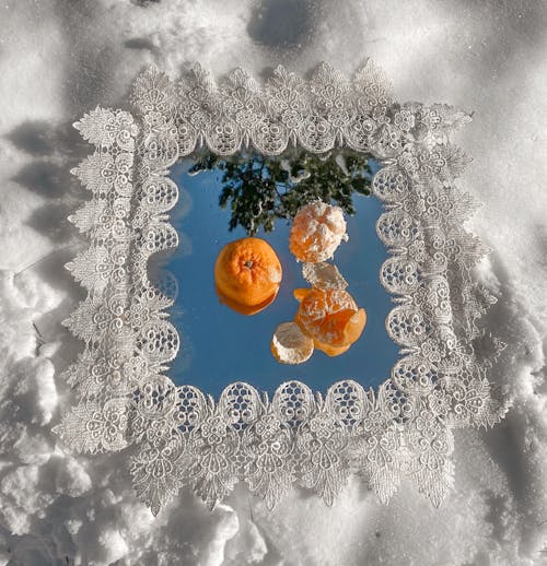 Mirror with tangerines on snowy ground in forest