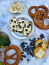 Top view of fresh baked food and loaf with cheese near pineapple with pomelo and scattered blueberries on white plaid
