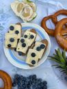 Top view slices of delicious loaf with cheese topped with ripe blueberries served on white plaid with fresh fruits during picnic