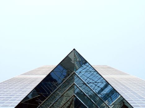 Low angle facade of modern multistory building with futuristic geometric design and glass walls and windows under blue cloudless sky in sunny day