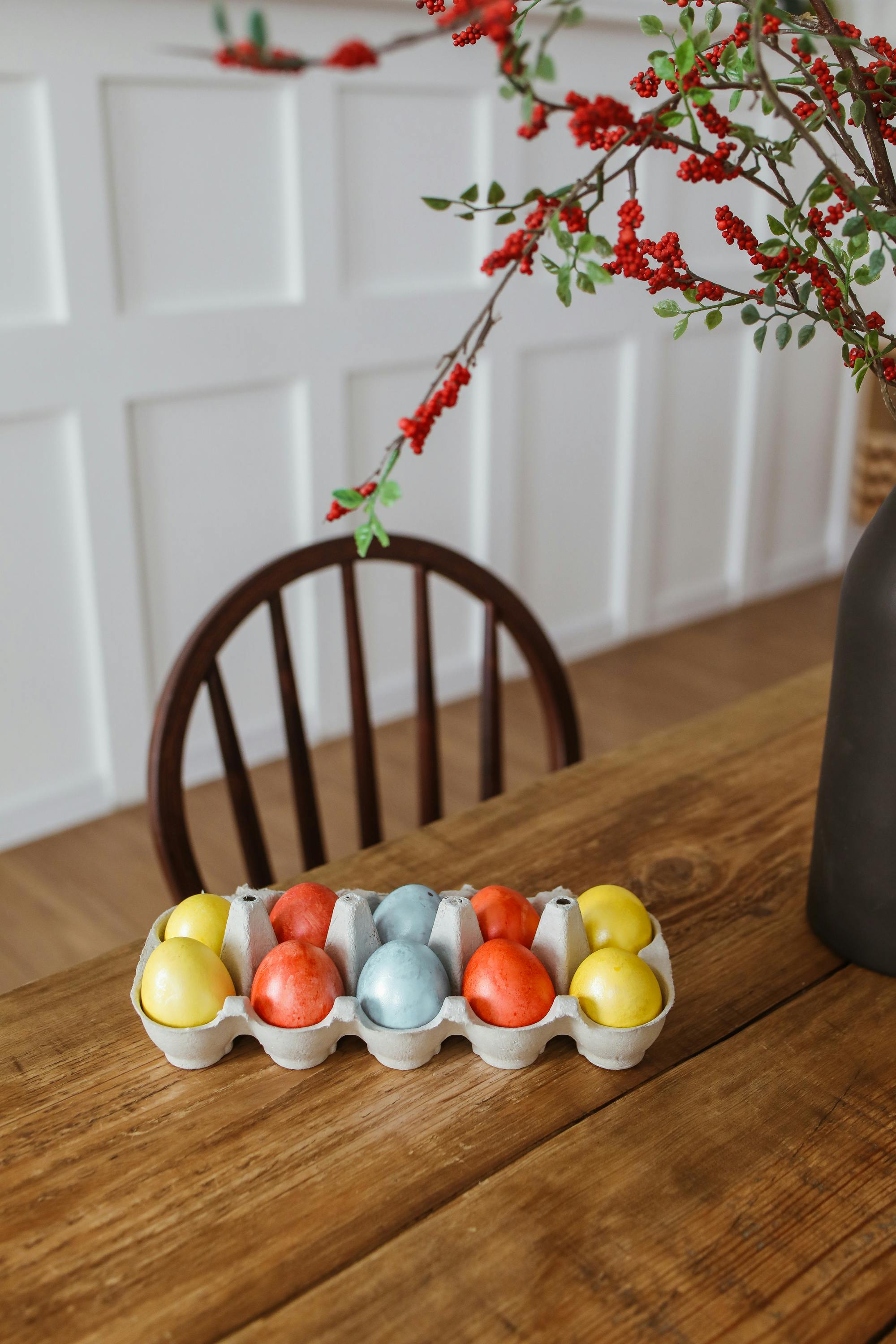 Colorful Easter eggs in an egg carton on a wooden table with floral decor.