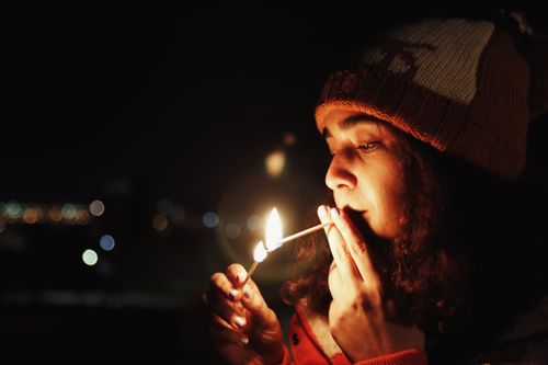 Free A woman in a beanie lighting a cigarette in the dark, vivid flame illuminating her face. Stock Photo