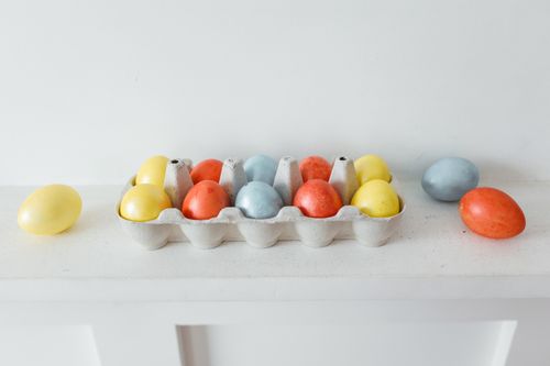 Free A carton of vibrant Easter eggs arranged on a white surface, showcasing holiday decoration. Stock Photo