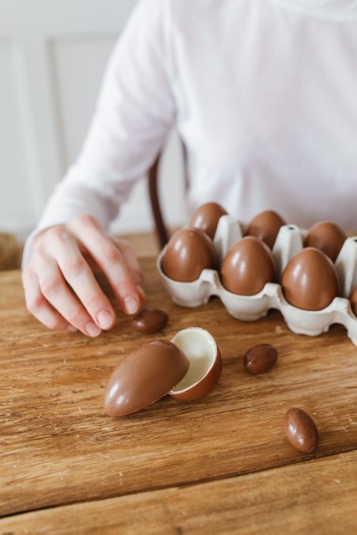 Free A hand reaches for chocolate eggs in a carton on rustic wood table. Stock Photo