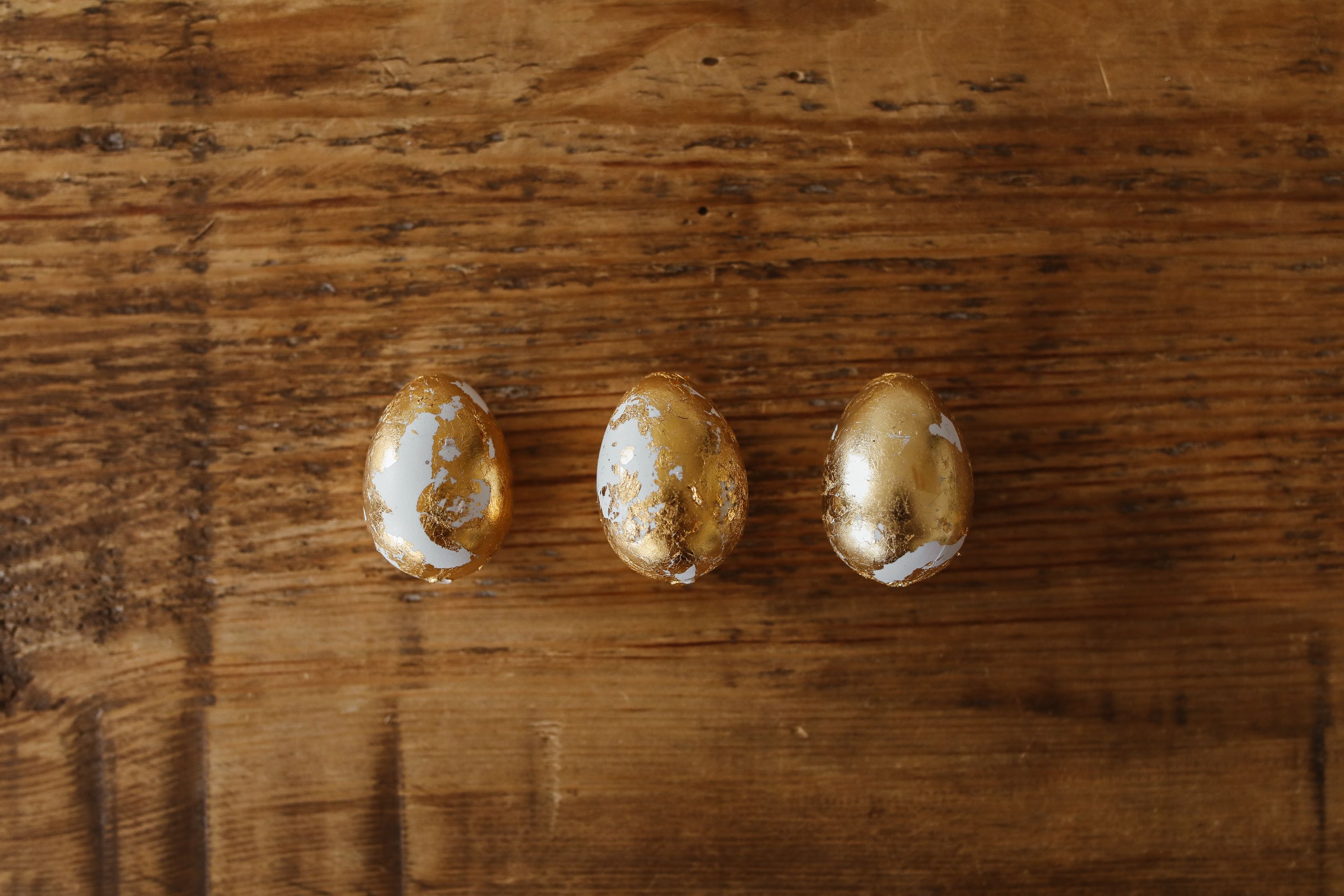Three golden Easter eggs on a rustic wooden table from an aerial view, perfect for holiday or decoration themes.