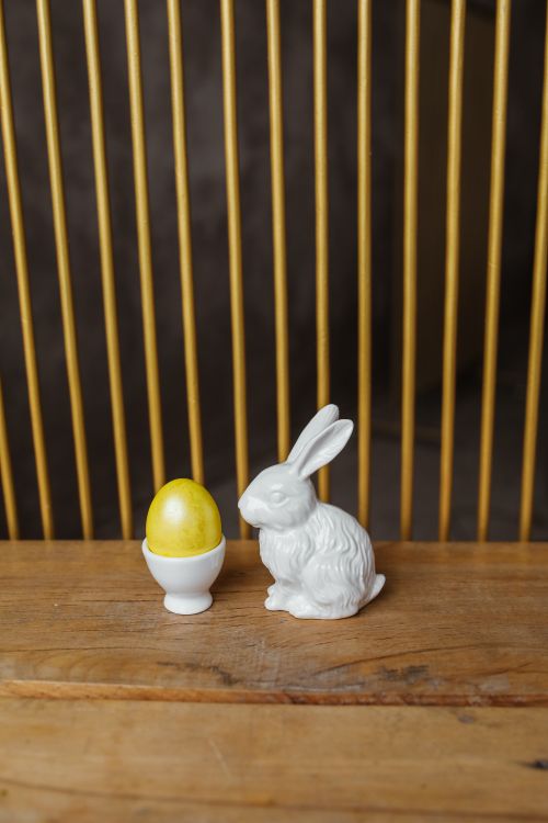 Free A decorative porcelain rabbit with a colorful egg on a wooden surface, perfect for Easter themes. Stock Photo