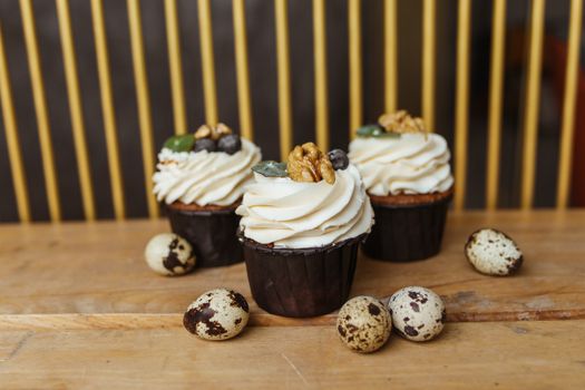 Close-up of gourmet cupcakes decorated with quail eggs and walnuts on a wooden surface.