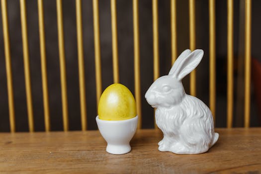 Easter bunny figurine beside a yellow egg in a holder on a wooden table.