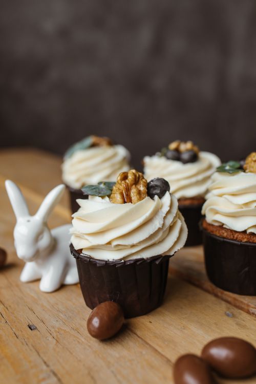 Free Easter-themed cupcakes with cream and walnut toppings beside a ceramic bunny figurine on a wooden surface. Stock Photo