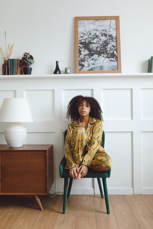 Free Woman in yellow pajamas sitting on a green chair in a cozy living room interior. Stock Photo