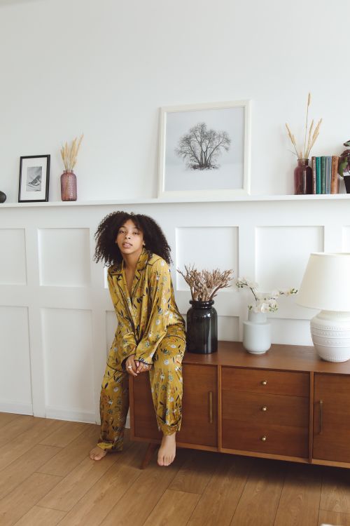 Free Woman in pajamas sitting on cabinet in cozy living room, featuring modern decor. Stock Photo