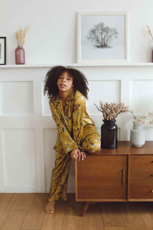 Free Woman in floral pajamas sitting on wooden cabinet in cozy indoor setting with decor. Stock Photo