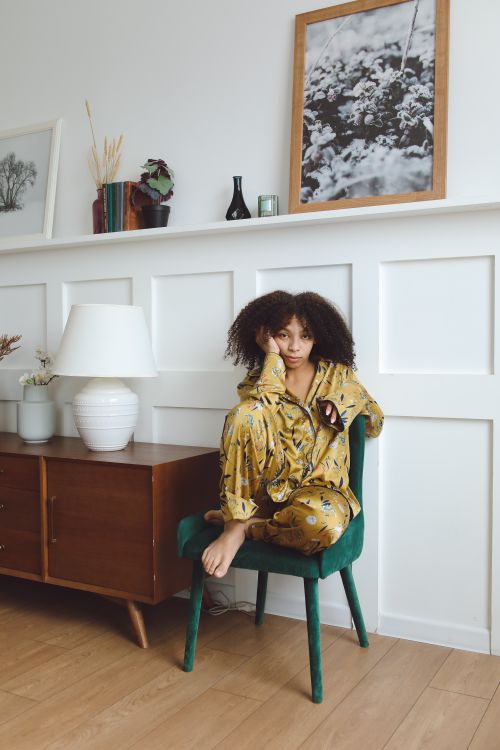 Free A woman in printed loungewear sits on a chair in a modern living room setting, exuding comfort and style. Stock Photo