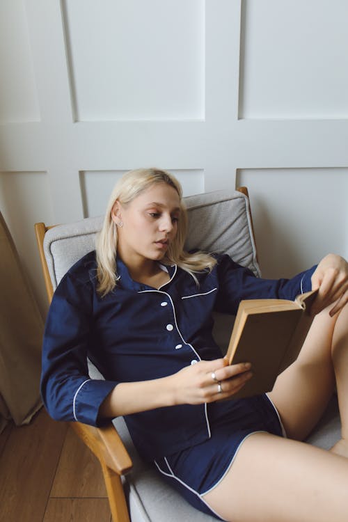 Blonde Woman Reading a Book Sitting on Wooden Armchair 