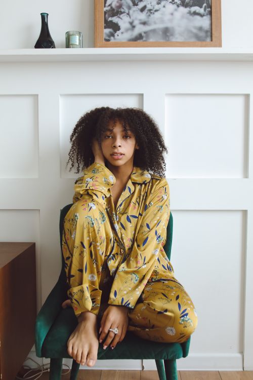 Free A woman with curly hair sits comfortably in colorful pajamas against a paneled wall. Stock Photo