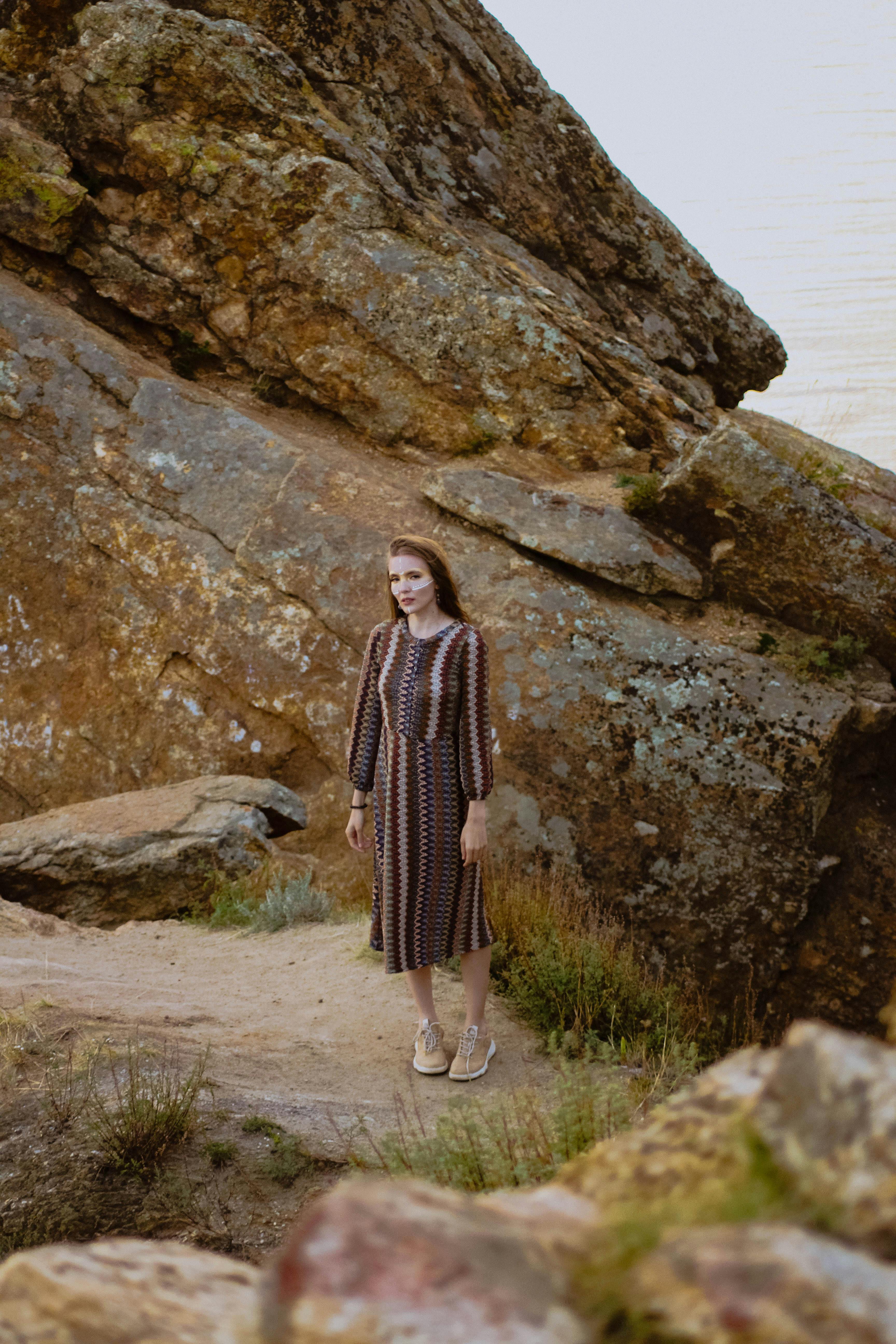 A woman in a patterned dress poses against a striking rocky formation, showcasing erosion patterns.