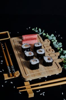 Sushi rolls with seaweed on a bamboo board, garnished with greenery and chopsticks.
