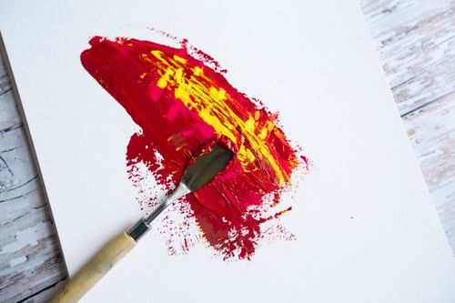 Free Top view of professional metal palette spatula placed on white canvas with smears of red paint placed on wooden floor Stock Photo