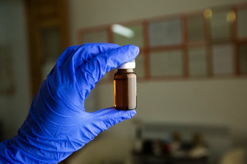 Unrecognizable doctor wearing glove standing in room with glass bottle of vaccine for injection on blurred background during coronavirus pandemic