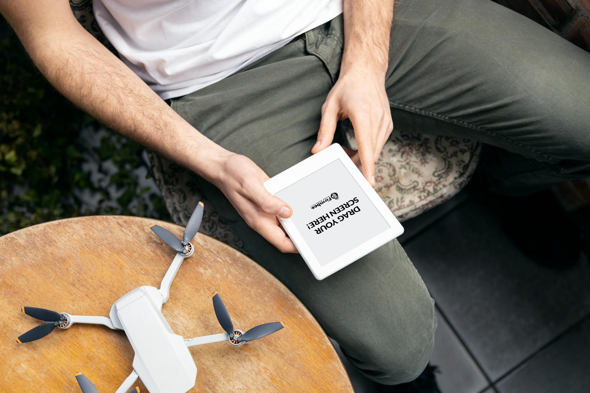 Close-up of a man holding a tablet with a drone on the table, ready for use.