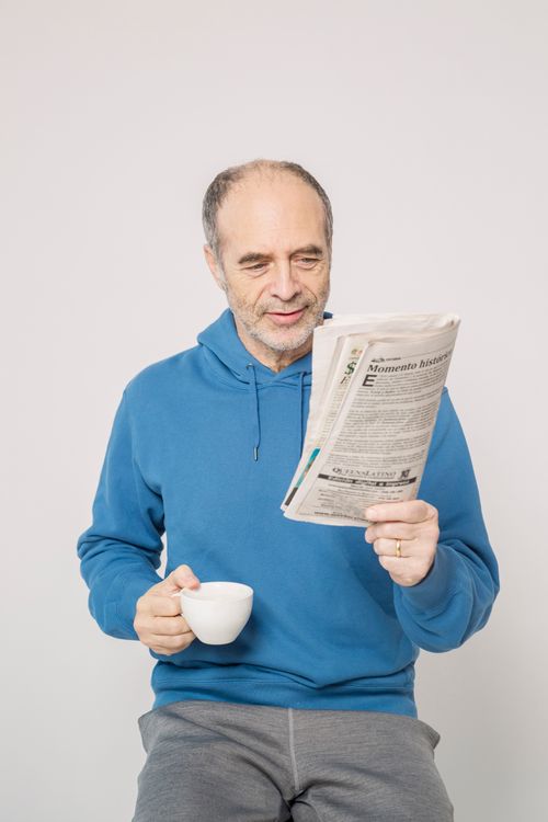 Free Elderly man in casual attire enjoying coffee and reading a newspaper indoors. Stock Photo