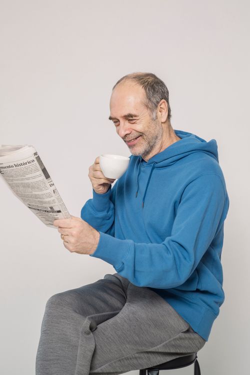 Free Elderly man in casual attire sipping coffee and reading a newspaper indoors. Stock Photo