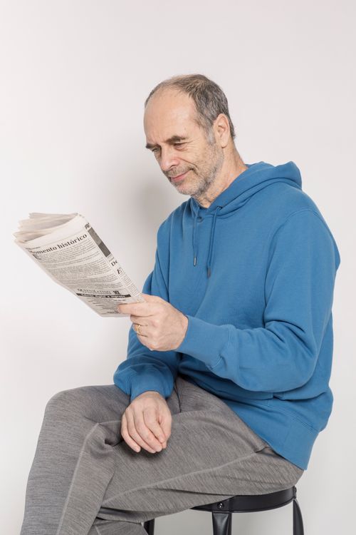 Free Senior man in blue hoodie reading a newspaper indoors Stock Photo