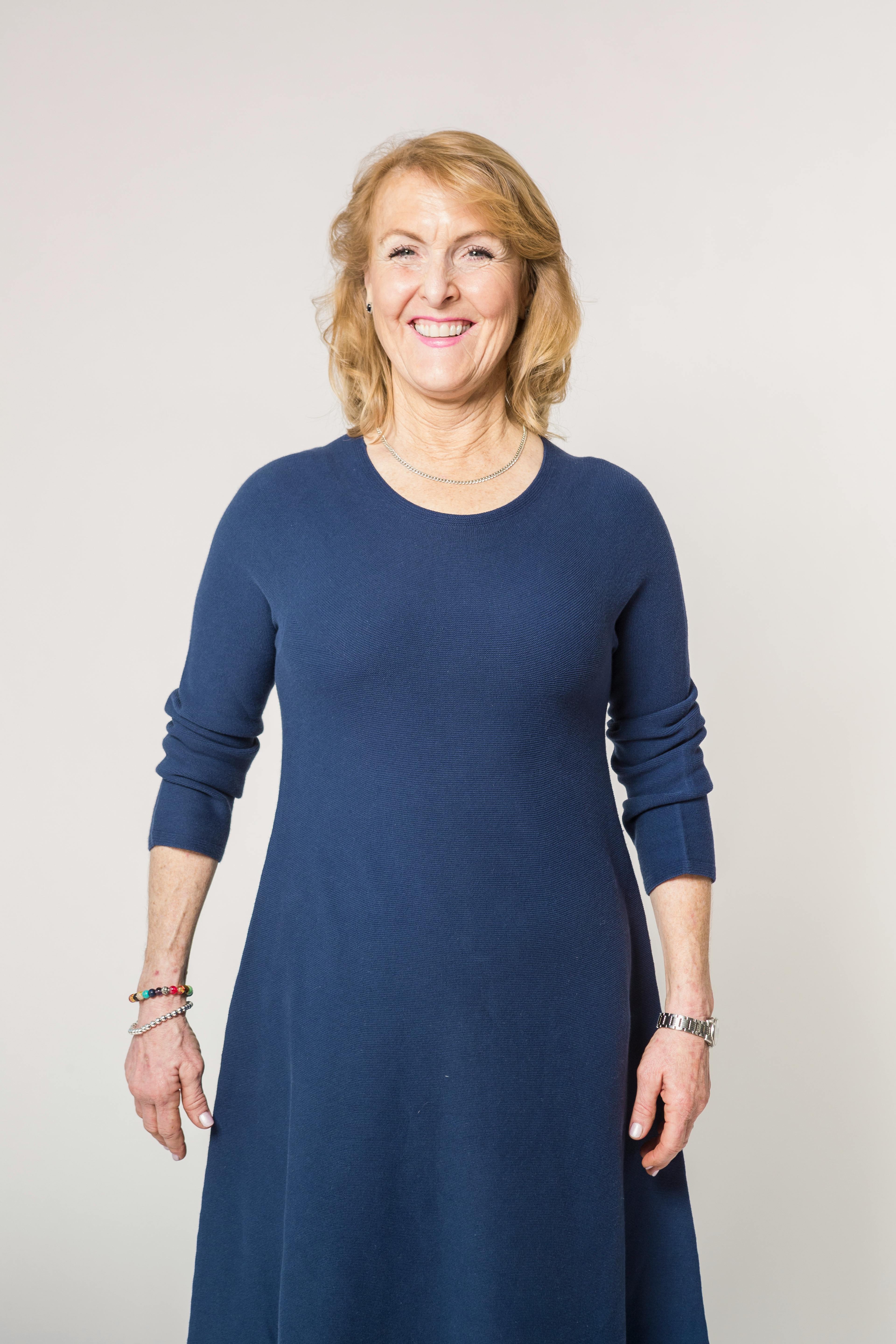 Portrait of a smiling elderly woman in a blue dress posing indoors.