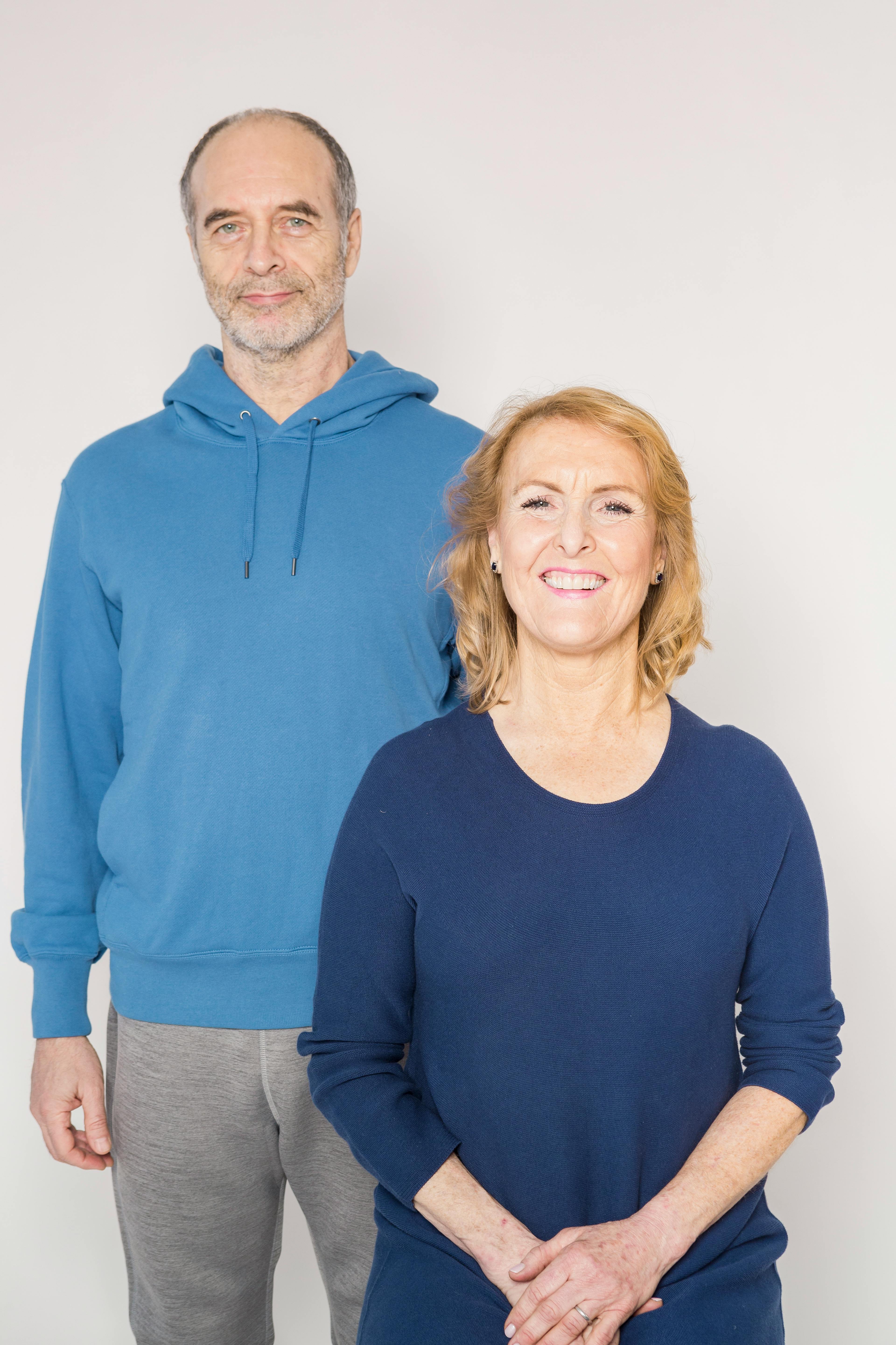 Happy senior couple posing and smiling indoors, dressed in casual blue attire.