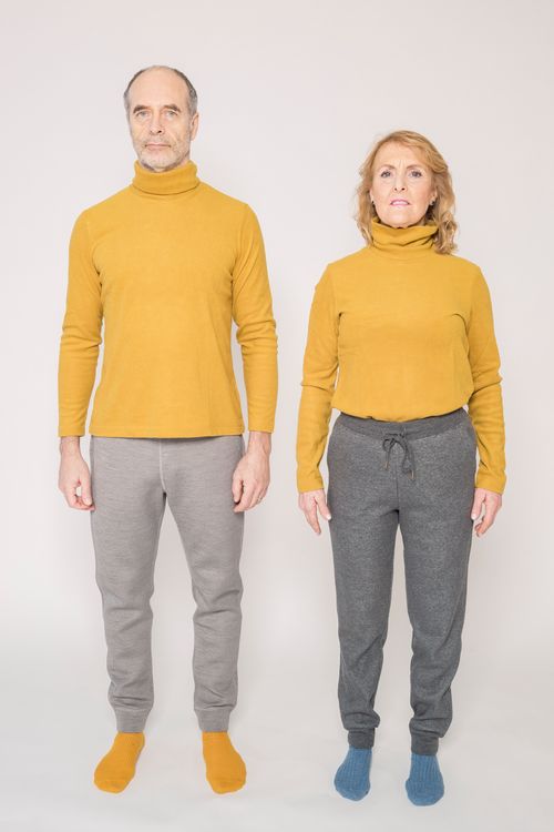 Free Senior couple in matching yellow sweaters posing seriously in a studio setting. Stock Photo