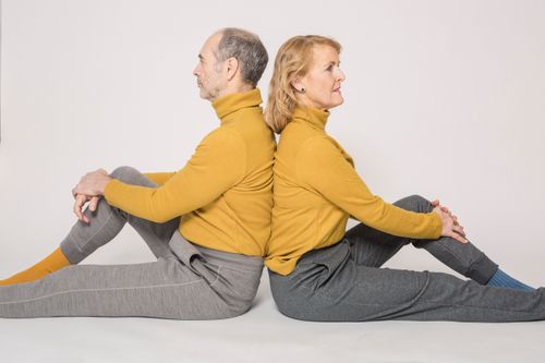 Free Elegant elderly couple in yellow sweaters posing back to back in a studio setting. Stock Photo