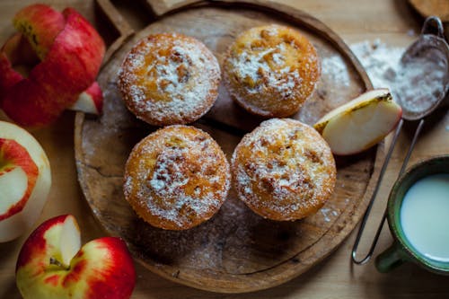 Top view of delicious baked muffins with powdered sugar placed near cut healthy apples in kitchen